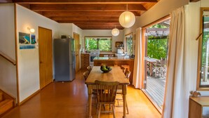 Une cuisine spacieuse avec des poutres en bois, un coin repas avec une table et des chaises en bois, et de grandes fenêtres offrant une vue sur l’extérieur.