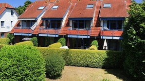 A row of terraced houses with balconies, a well-maintained garden, and a clear blue sky. - Papillon Whg. 06/1, Germany (Ostseebad Boltenhagen)