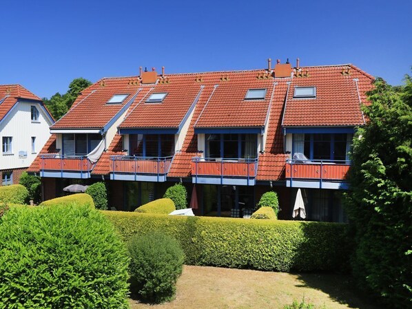 A row of terraced houses with balconies, a well-maintained garden, and a clear blue sky.