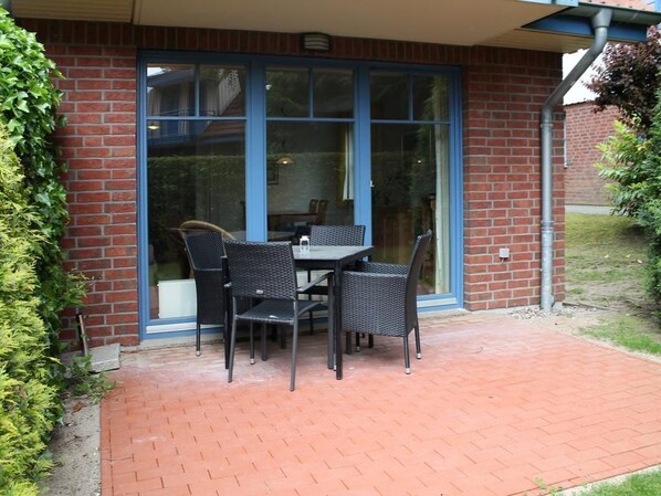 A patio with a table and chairs, a brick wall, and a glass door.