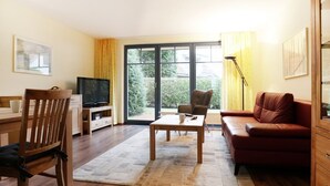 A living room with a wooden floor, a sofa, a television, a coffee table, and a window with curtains. - Papillon Whg. 06/1, Germany (Ostseebad Boltenhagen)