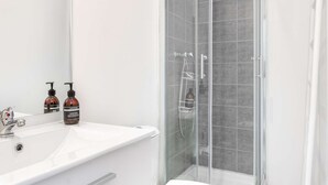 A modern bathroom with a glass-enclosed shower, a white sink, and two hand wash bottles. - MaisonMars Studio 5 Blancarde (Marseille)
