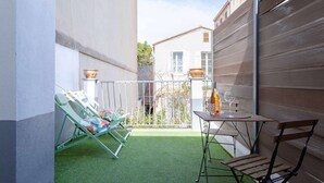 A small outdoor patio with a green artificial turf, a metal table with two chairs, and a wooden bench. - MaisonMars Studio 5 Blancarde (Marseille)