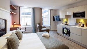 A modern hotel room with a large bed, a sitting area with a chair, a flat-screen TV, a microwave, and a small kitchen area. - Charlotte Rise (Bristol)
