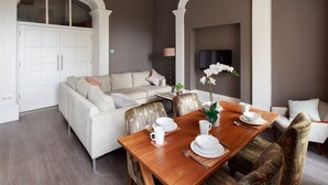 A dining area with a wooden table set for four, surrounded by patterned chairs. A white sofa and a television are visible in the background. - Charlotte Rise (Bristol)