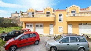 A yellow building with two balconies, a red car, and a silver car parked in front. - Two Bedroom Apartment with Balcony (Kaštel Stari)