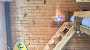 Un interior de madera con una litera, una lámpara con forma de estrella y una tabla de surf apoyada contra la pared.