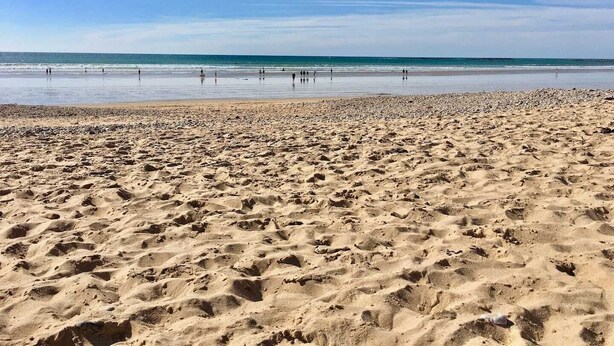 Una extensa playa arenosa con huellas y un cielo azul despejado.