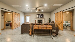 Un salón espacioso con chimenea, ventilador de techo y una gran mesa de madera.