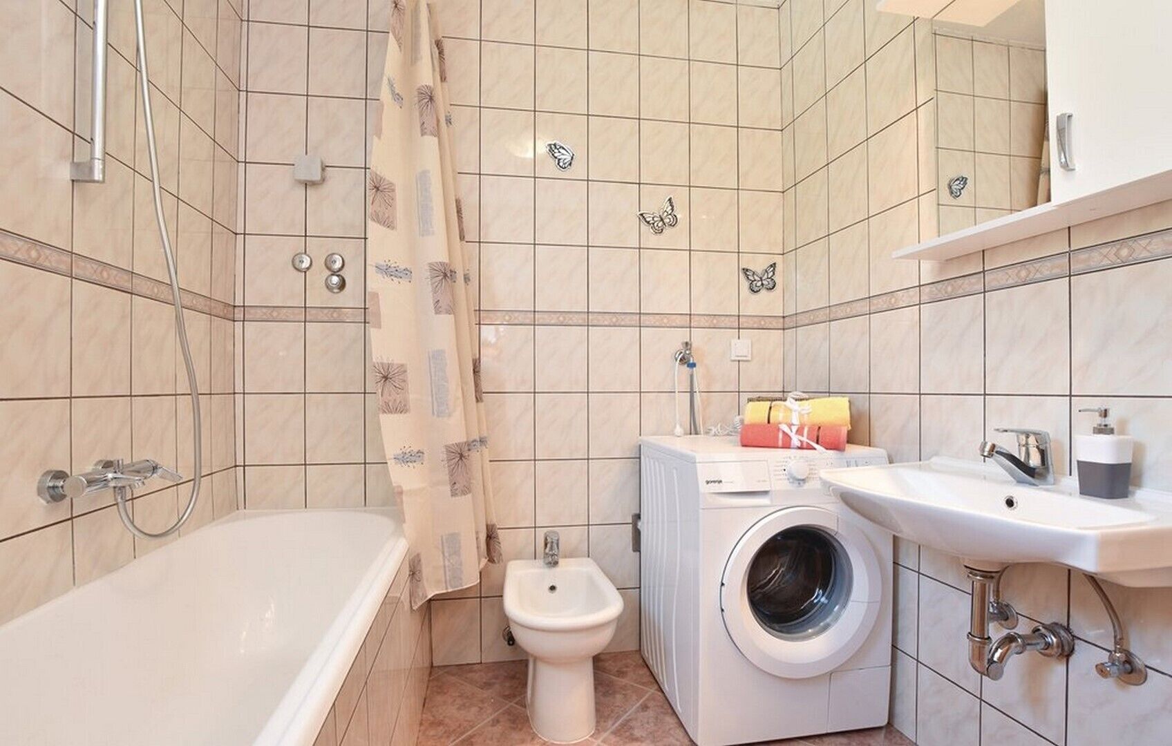 Een kleine badkamer met bad, toilet, wasmachine en wastafel.