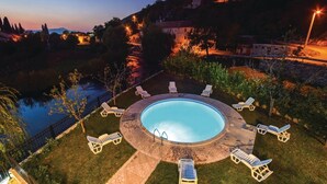 Una piscina circolare con lettini prendisole intorno, circondata da un solarium in pietra e una recinzione.