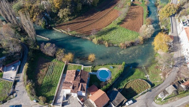 Una vista aerea di una zona residenziale con un fiume, campi a terrazze e una piscina.