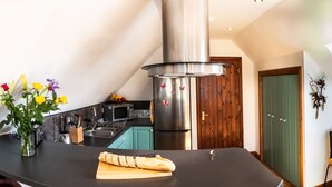 A modern kitchen with a central island, a microwave, and a refrigerator. There is a wooden door and a window with a view of the sky.