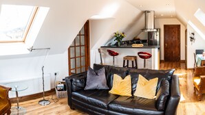 A spacious loft apartment with a black leather sofa, a wooden dining table, and a kitchen area.
