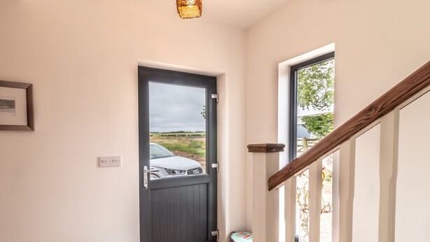 A modern interior with a dark wooden door, a staircase with white balusters, and a view of a white car outside.