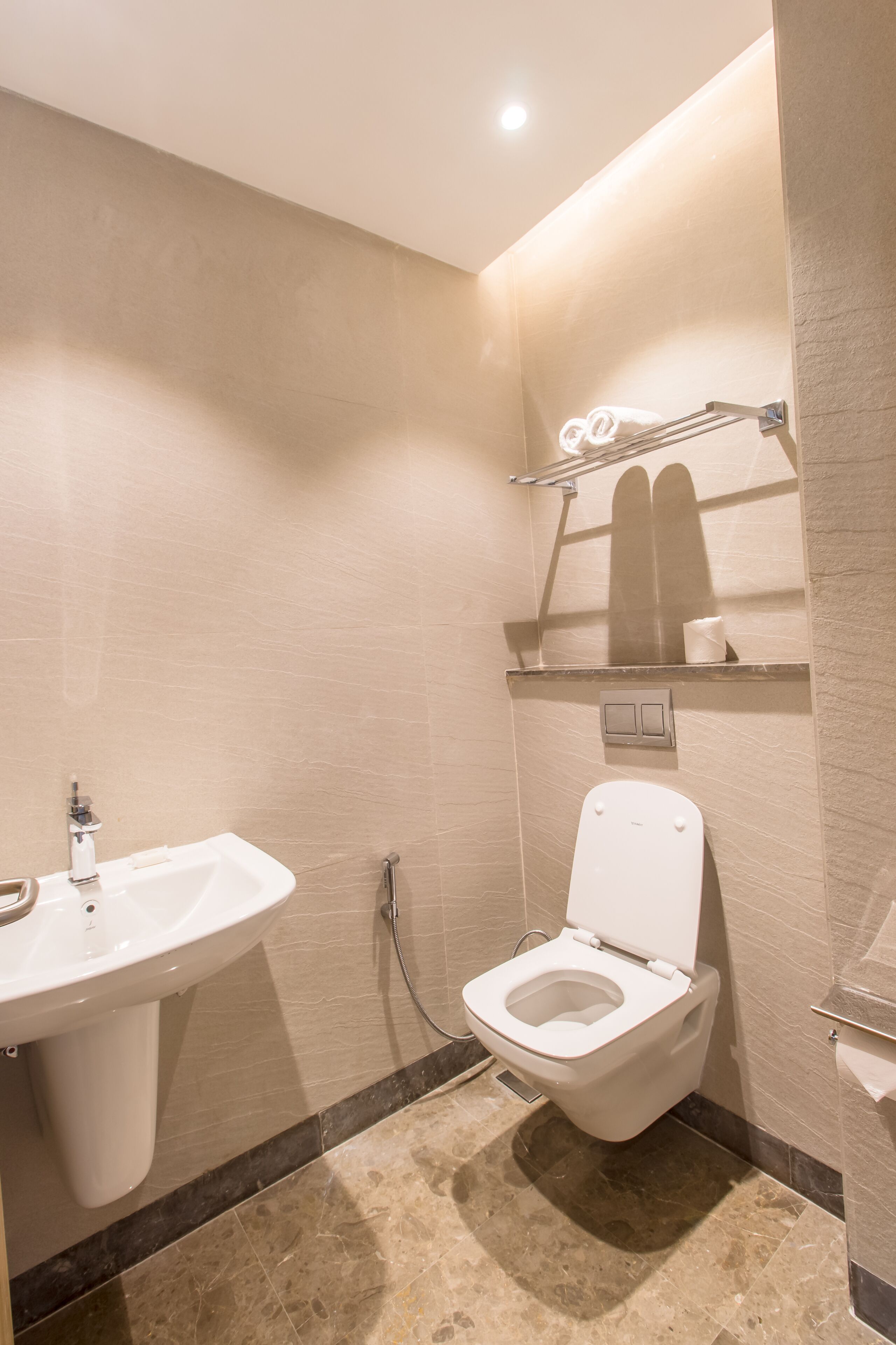 A modern bathroom with a white sink, toilet, and shelves above the toilet.