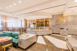 Un moderno vestíbulo de hotel con área de descanso, una recepción y un amplio ventanal.