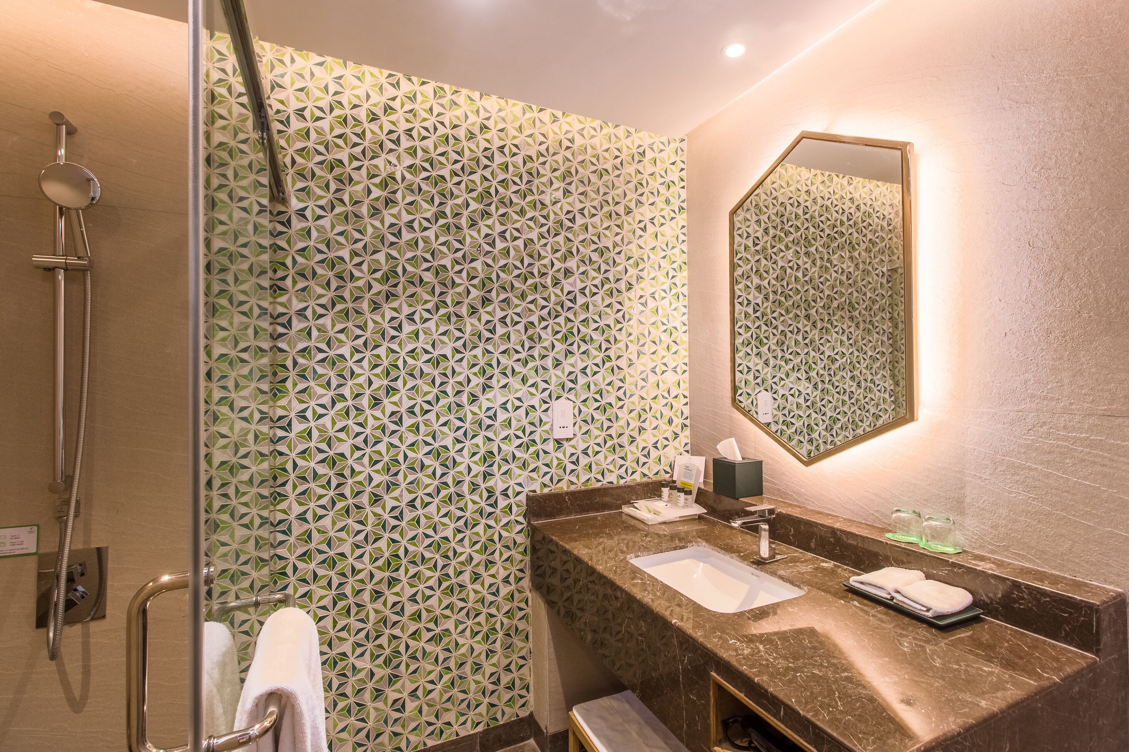 Un baño con ducha, lavamanos con espejo y pared con diseño.