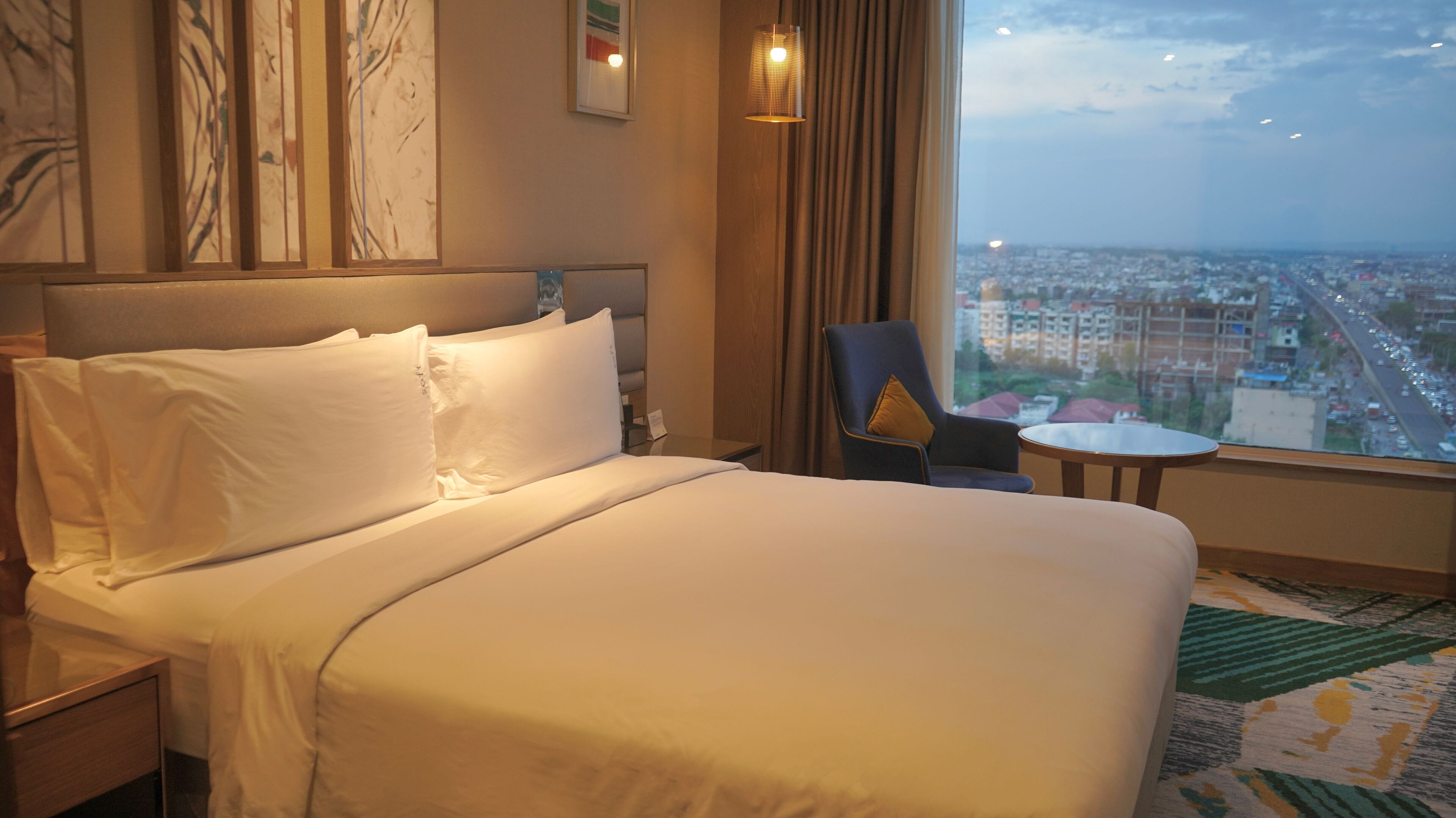 Una camera d'albergo con un letto, una sedia, un tavolino e vista sulla città attraverso la finestra.