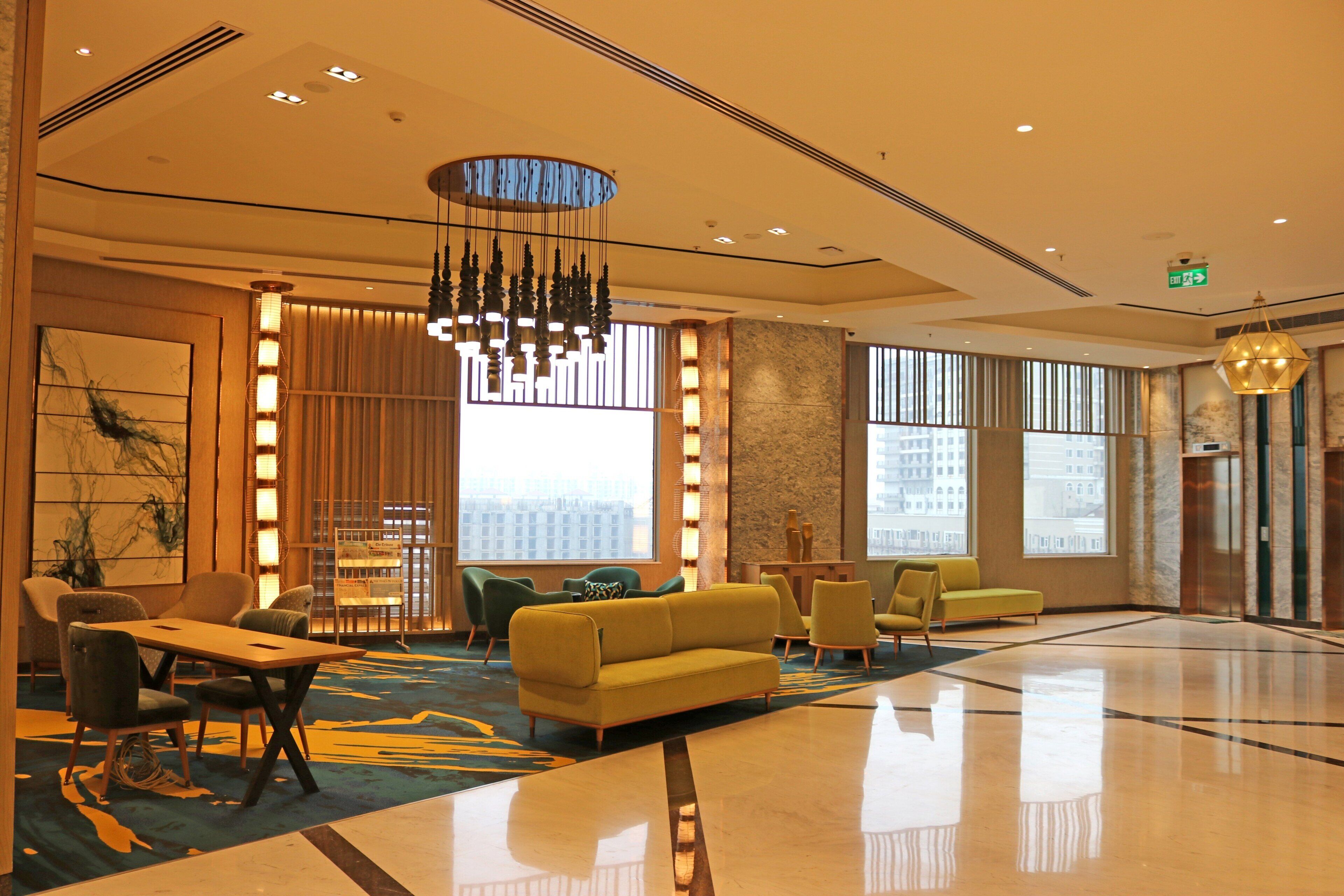A spacious lobby with a modern chandelier, seating area, and large windows offering a view of the cityscape.