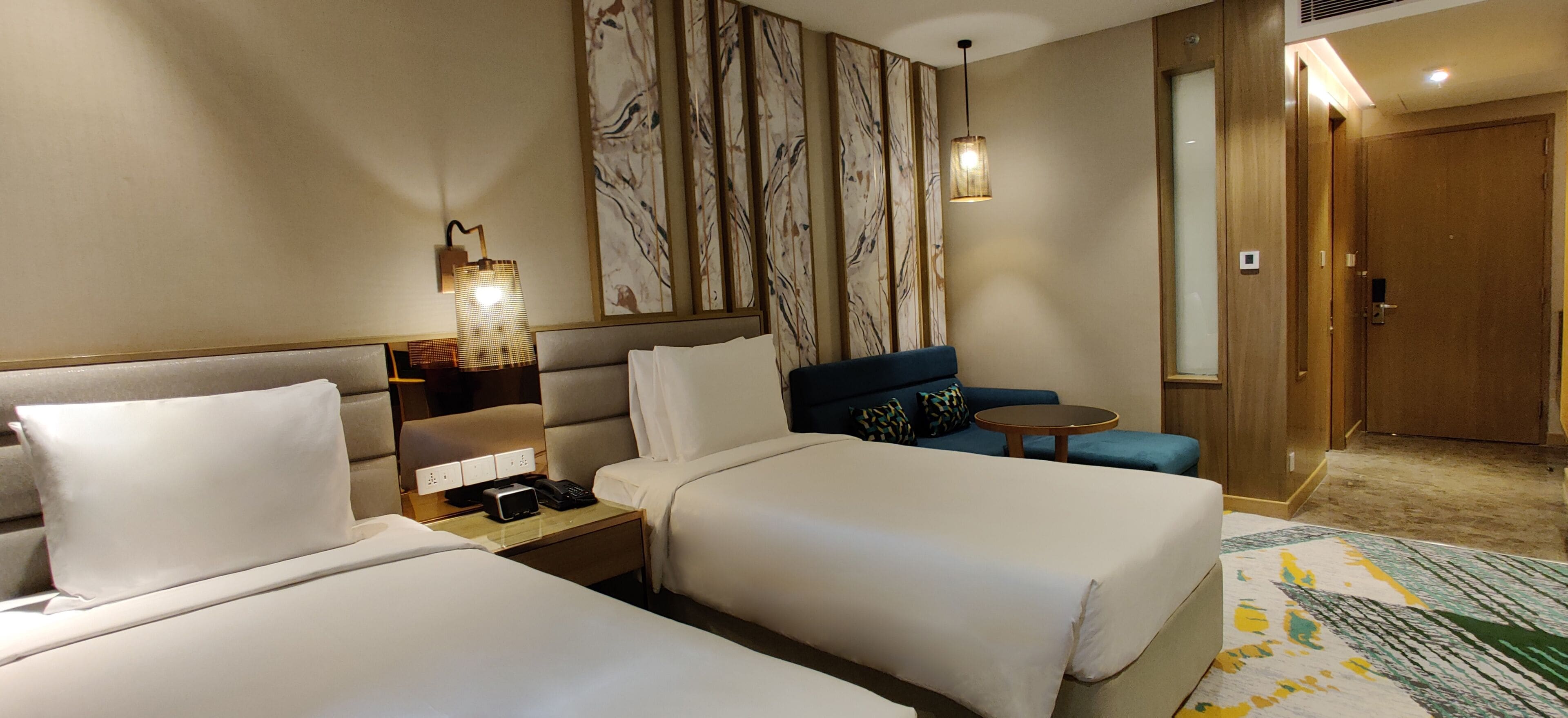 A hotel room with two beds, a sofa, a small table, and a wall with abstract art.