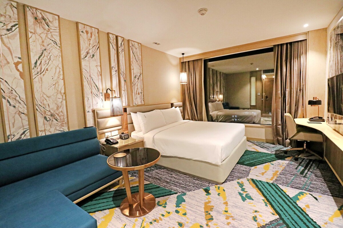 A hotel room with a bed, a sofa, a desk, and a mirror.