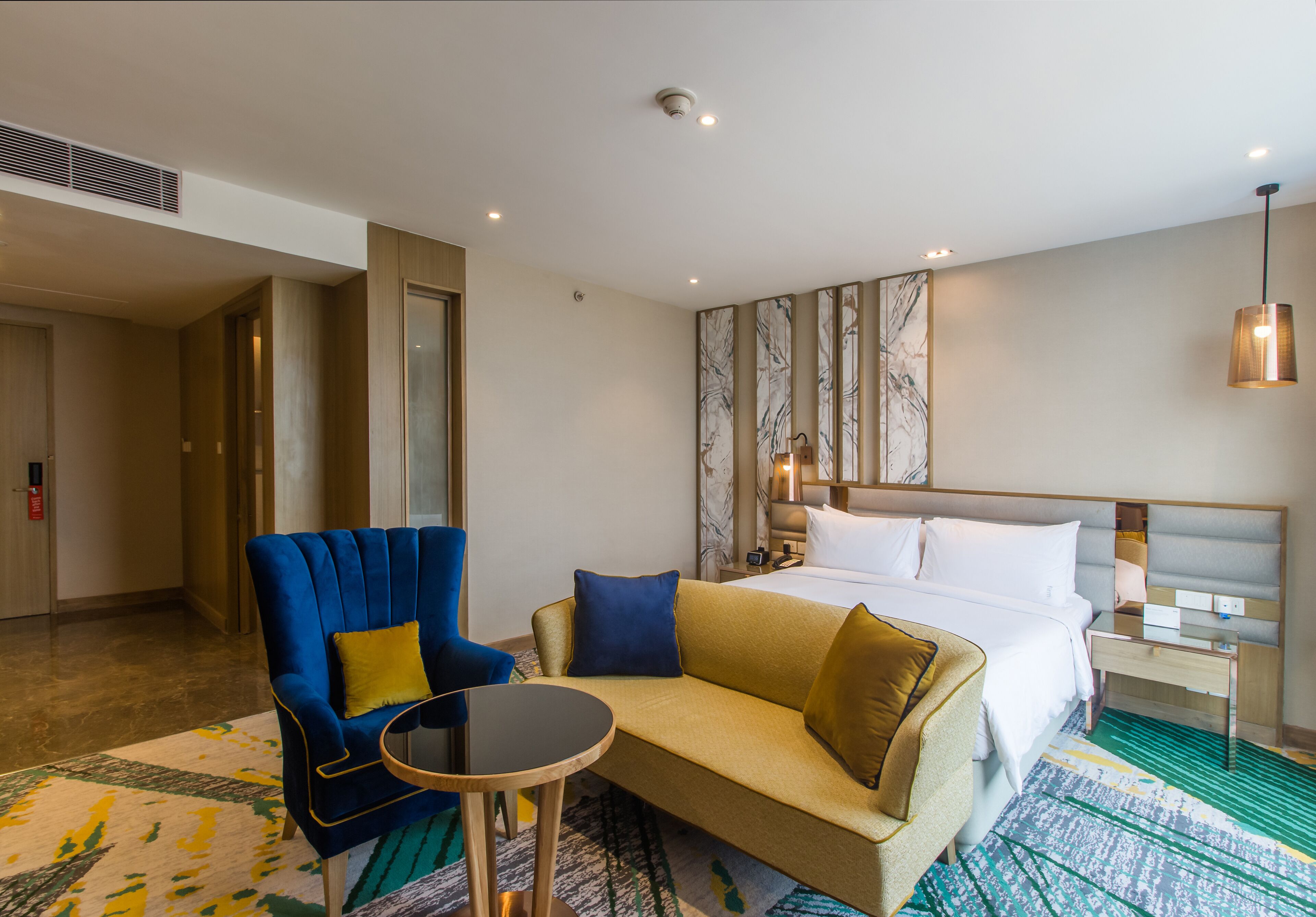 A hotel room with a bed, a sofa, a chair, a small table, and a patterned wall.