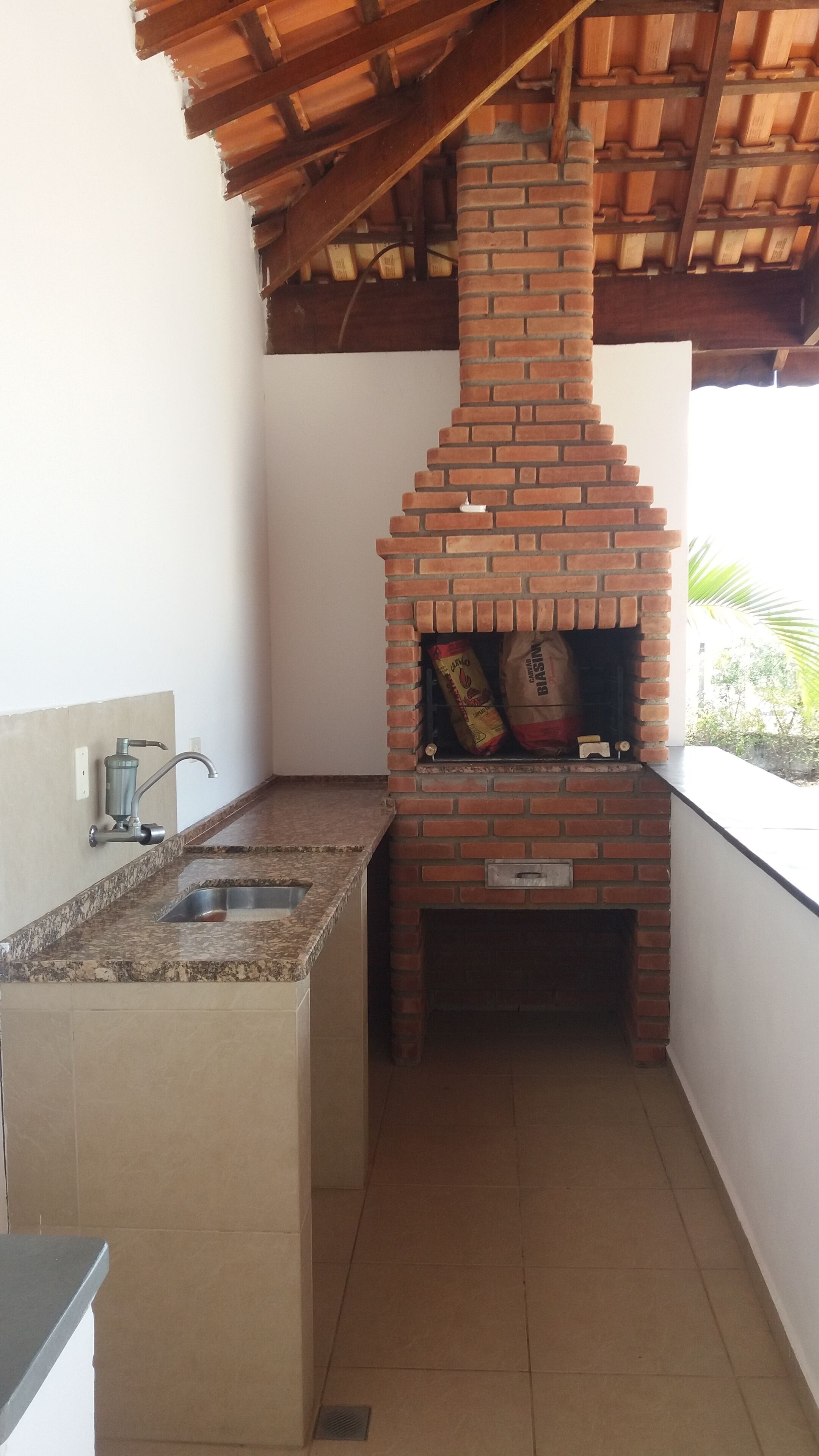 A kitchen with a brick oven, a sink, and a window overlooking greenery.