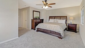 Um quarto com cama, mesas de cabeceira, cômoda, ventilador de teto e espelho.
