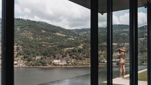 Vista de um edifício moderno com grandes janelas sobre um lago e uma paisagem montanhosa.