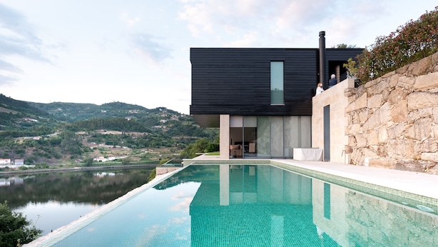 Uma casa moderna com piscina, muro de pedra e vista para a paisagem ao redor.