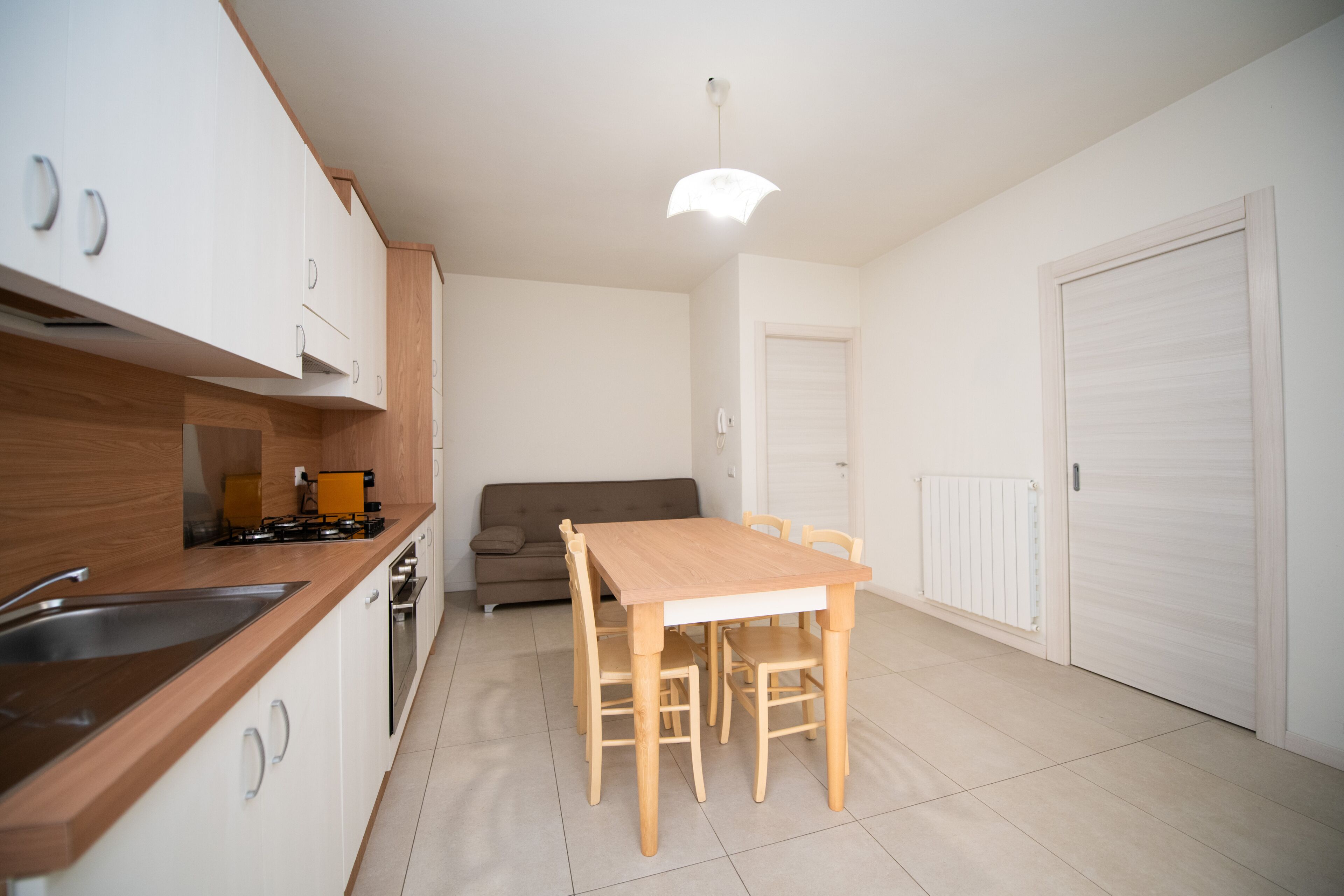 A compact kitchen with a wooden table and chairs, a built-in oven, and a sink.