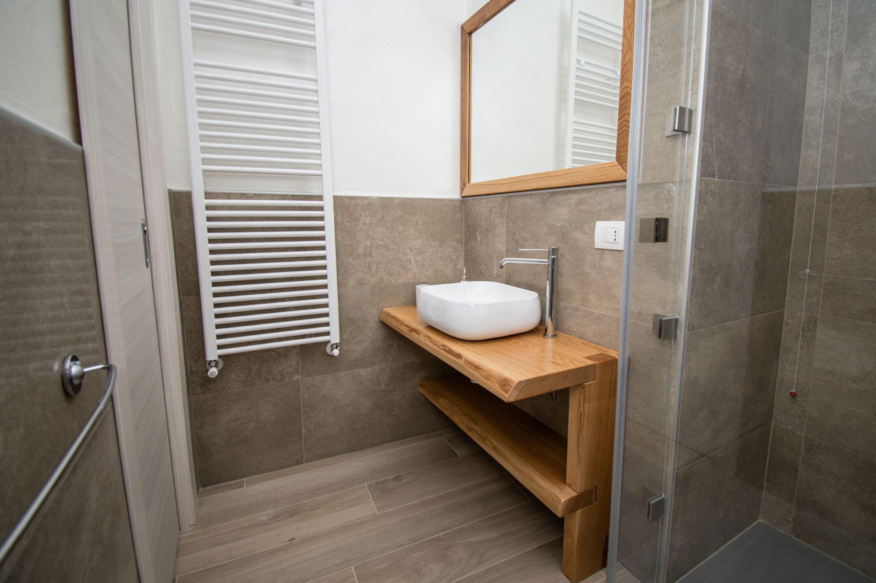 A modern bathroom with a wooden vanity, a white sink, and a glass shower enclosure.