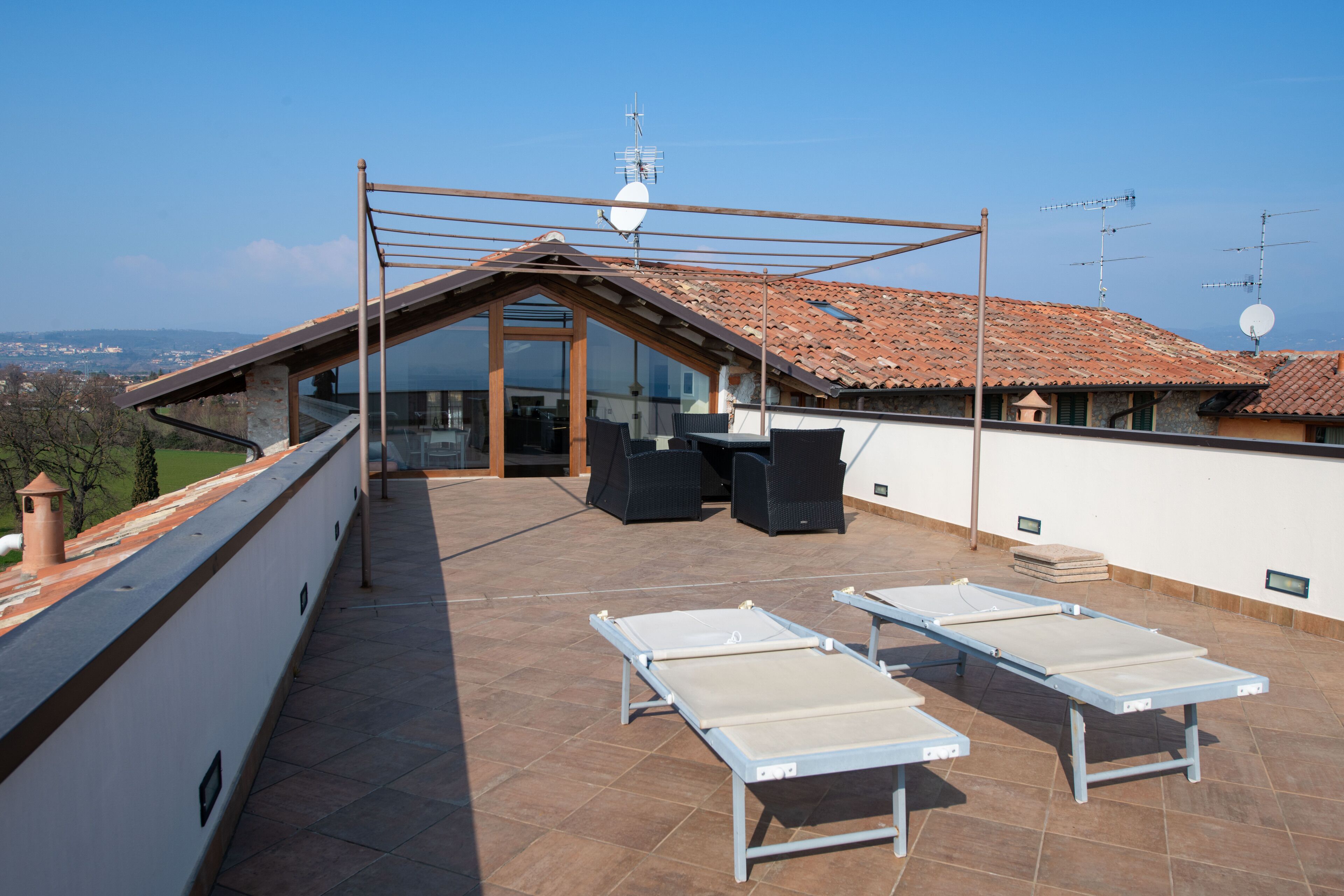 Eine Dachterrasse mit Glasveranda, zwei Liegestühlen und Blick auf die Stadt.