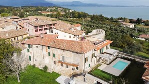Un edificio de piedra con piscina, rodeado de vegetación y vistas a un lago.