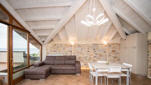 Un interior moderno con una pared de piedra, un sofá seccional marrón, una mesa de comedor blanca con sillas y un ventanal con vistas.