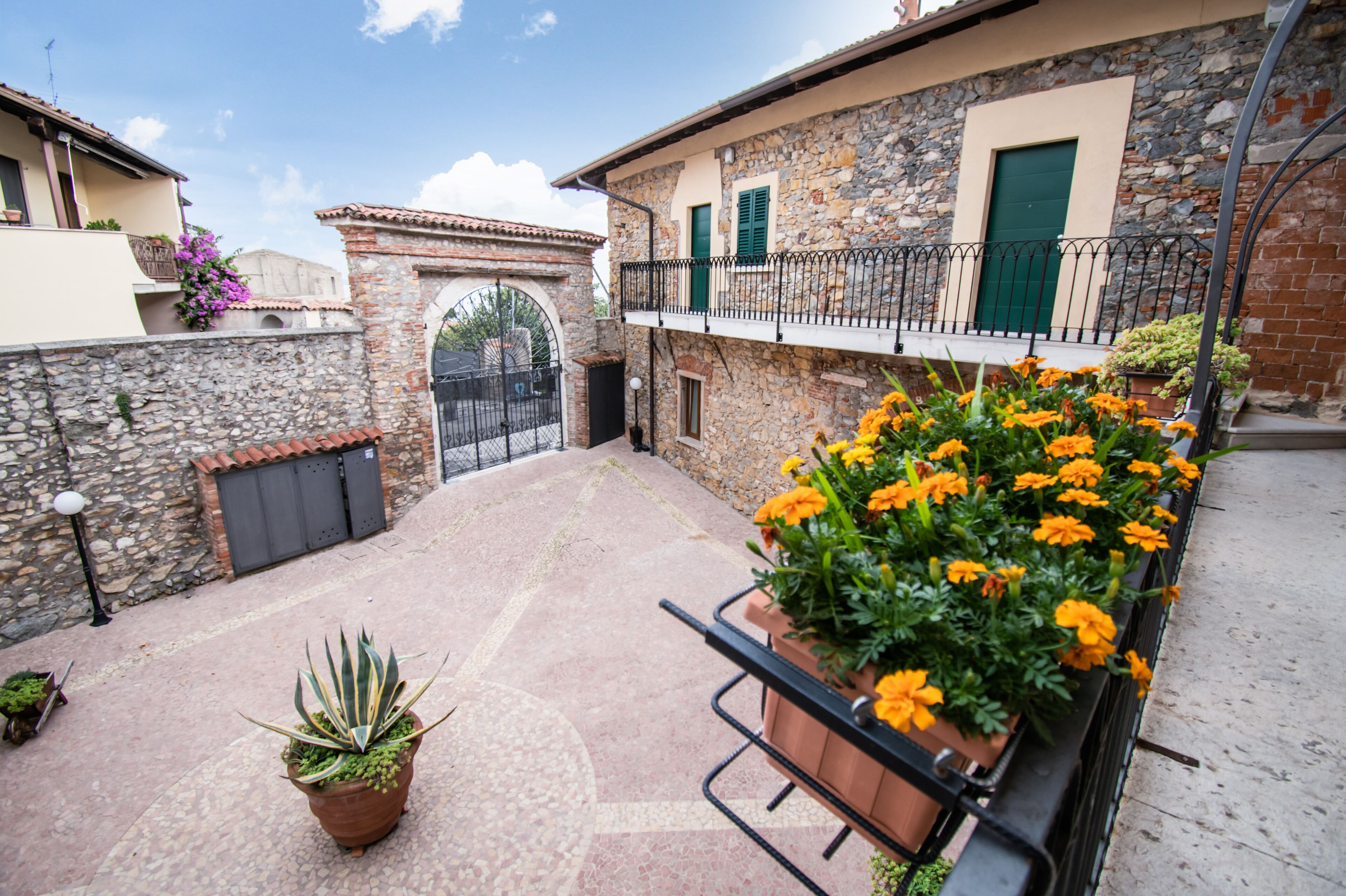 Un patio con muros de piedra, una reja y plantas en macetas.