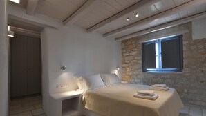 Un dormitorio moderno con una pared de piedra, una cama con sábanas blancas y una ventana con persianas.
