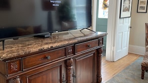 Ein großer Flachbildfernseher auf einer Holzkabinet mit Schubladen, platziert in einem Raum mit einer Tür und gerahmten Bildern an der Wand.