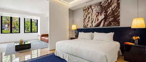 A modern hotel room with a large bed, two bedside lamps, a wall-mounted artwork, and a view through large windows.