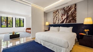 A modern hotel room with a large bed, two bedside lamps, a wall-mounted artwork, and a view through large windows.