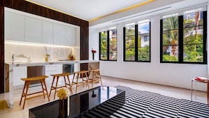 A modern kitchen with white cabinets, wooden stools, and a black and white striped rug.