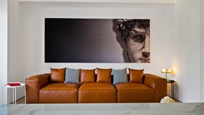 A modern living room with a brown leather sofa, a large abstract painting, a small side table, and a floor lamp.