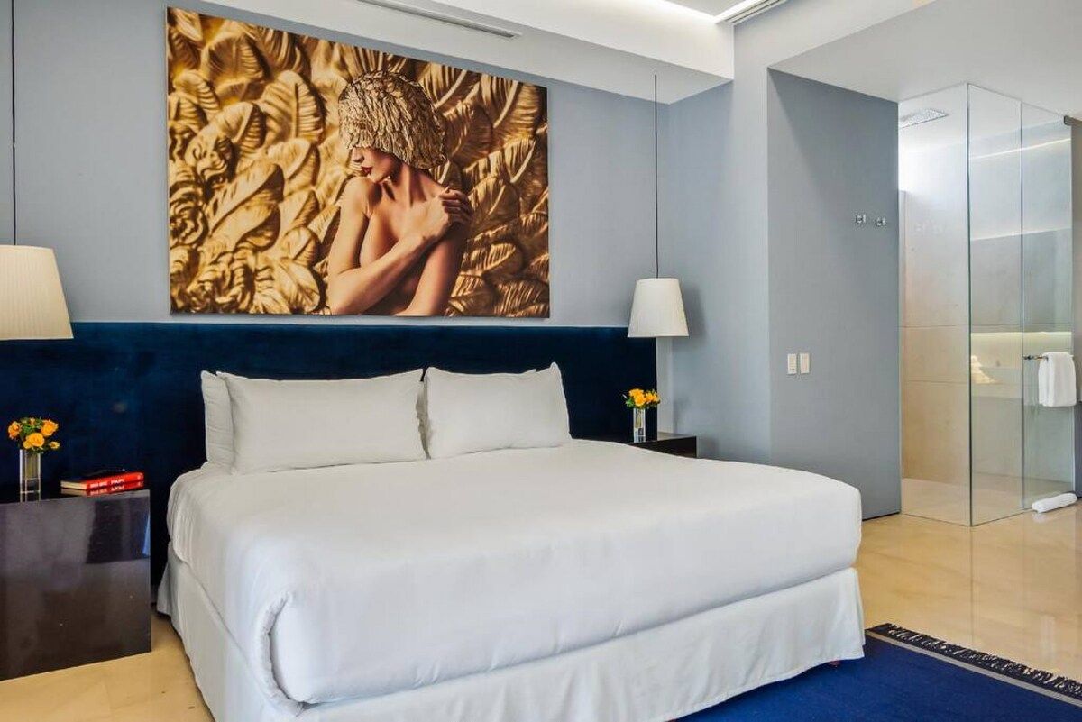 A modern hotel room with a large bed, a glass shower enclosure, and a decorative wall piece.