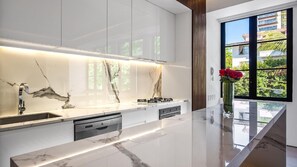 A modern kitchen with marble countertops, integrated appliances, and a view of greenery outside.