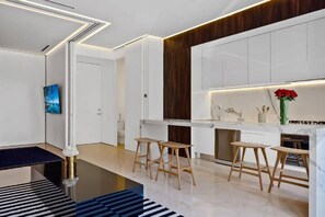 A modern kitchen with white cabinets, wooden stools, and a marble countertop.