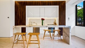 A modern kitchen with a marble countertop, wooden stools, and a vase with red flowers.