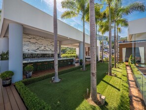 A modern outdoor area with a wooden deck, green lawn, and tall palm trees.