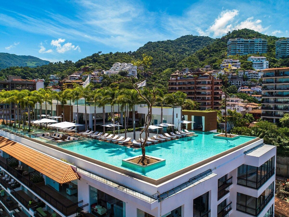 Una piscina en la azotea con tumbonas y vistas a un paisaje montañoso.