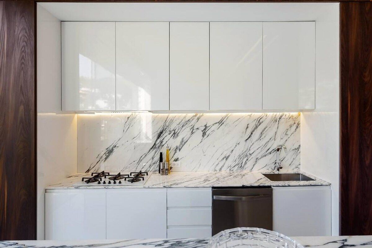 A modern kitchen with white cabinets, a marble backsplash, and stainless steel appliances.